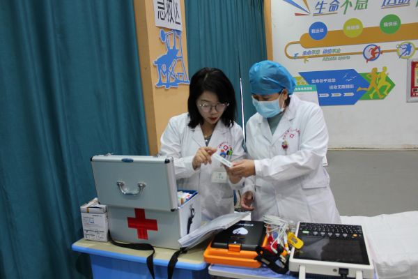 图为十二团医院副院长刘瑜（左）在十二团中学体育馆麻腮风接种急救区查看急救物品及急救设备。.JPG